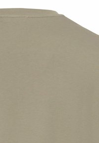 Beżowa koszulka z gładką fakturą, z okrągłym dekoltem i subtelnym detalem przeszycia przy kołnierzu.