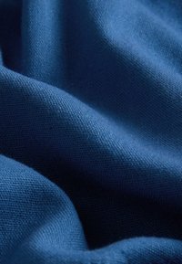 Prim-plan al unui material albastru moale, texturat, cu un model de țesătură vizibil și cute ușoare care creează umbre și zone luminoase.