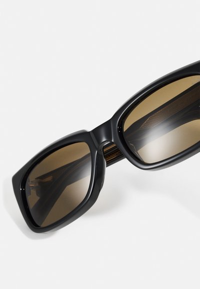 Schwarze, übergroße Sonnenbrillen mit einer eleganten Form, braun getönten Gläsern und strukturierten Innenrahmendetails. Kunststoffmaterial mit glänzender Oberfläche.