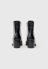 Stivali neri in pelle alla caviglia con una finitura lucida, cerniere laterali e un tacco spesso. Design semplice senza motivi o dettagli visibili.