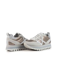 Le sneakers grigio chiaro presentano un mix di camoscio e dettagli metallici, una suola bianca spessa con battistrada a zigzag e lacci piatti.