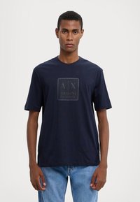 Camiseta de color navy con escote redondo y mangas cortas, con un diseño de logo texturizado en el centro. Fabricada en algodón. Corte casual.
