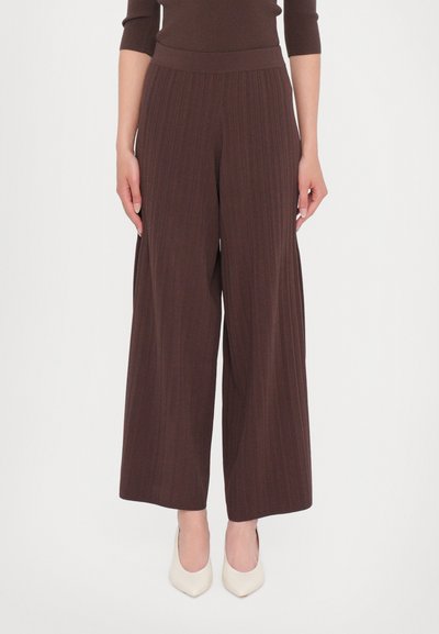 Pantalons évasés en tissu côtelé marron foncé, avec une taille haute et une coupe ample, associés à des escarpins pointus blancs cassé.