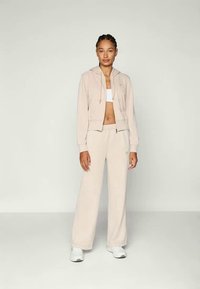 Sudadera corta beige con cordones, combinada con pantalones anchos a juego. La tela parece suave y transpirable. Zapatillas deportivas blancas completan el look.