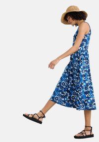 Blue floral dress with a fitted bodice and flowing skirt, paired with black strappy sandals and a straw hat.