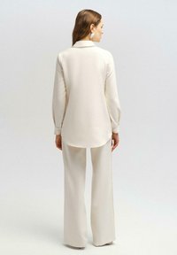 Cream silk blouse with a collar, long sleeves, and buttoned cuffs, paired with matching wide-leg trousers, creating a coordinated outfit.