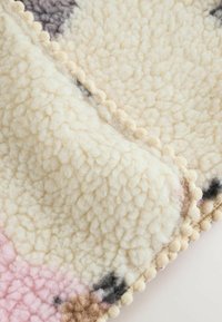 Weiches, cremefarbenes Gewebe mit flauschiger Textur, verziert mit einem rosa- und braunfarbenen Muster. Mit einem kleinen, runden Pomponabschluss versehen.