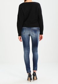 Suéter negro de pelaje suave combinado con jeans ajustados azul oscuro, con bolsillos traseros y ligero desgastado, complementado con zapatos de tacón negros.
