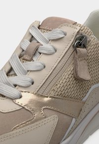 Μπεζ και ανοιχτό ροζ αθλητικά παπούτσια με συνδυασμό δέρματος, διχτυωτού υφάσματος και μεταλλικών λεπτομερειών. Λευκά κορδόνια και πλευρικό φερμουάρ προσθέτουν λειτουργικότητα και σχεδιασμό.