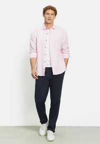 Lichtroze linnen shirt met lange mouwen, dichtgeknoopt, gecombineerd met marineblauwe broek en witte sneakers. Geen zichtbare patronen of accenten.