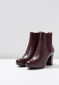 Burgundy leather ankle boots with a smooth finish, elastic side panels, and a block heel. Rounded toe and minimalistic design.