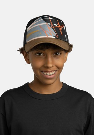 Lächelnde junge Person mit Zahnspange, trägt ein schwarzes Shirt und eine mehrfarbige Kappe mit abstrakten orangefarbenen und weißen Mustern.