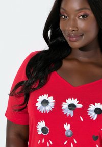 Rotes V-Ausschnitt-T-Shirt aus weichem Stoff mit weißen und grauen Gänseblümchen mit schwarzen Zentren, die auf der Vorderseite in einem Muster angeordnet sind.