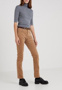 Graues, kurzärmliges Rollkragenoberteil kombiniert mit hellbraunen Cordhosen. Brauer Gürtel mit einer runden Goldschnalle. Schwarze Schnürschuhe.