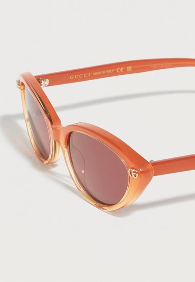 Lunettes de soleil orange translucide style œil de chat avec des verres foncés et un petit logo Gucci en or dans le coin de la monture.