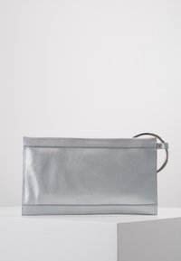 Rektangulär silvrig kuvertväska med slät yta, sydda kanter och ett stort metalliskt cirkulärt handtag på höger sida.