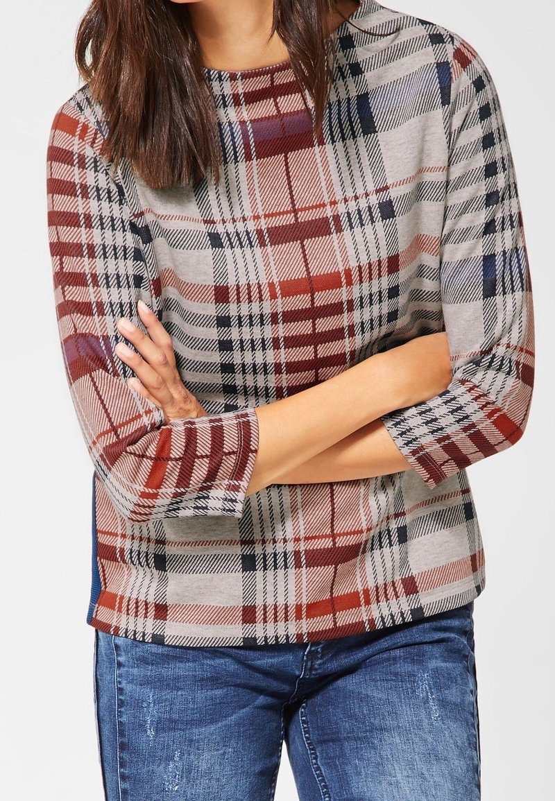 Haut à manches longues en tartan beige, rouge et bleu marine. Tissu doux avec un col rond et une coupe légèrement ajustée. Comporte des panneaux latéraux contrastants.