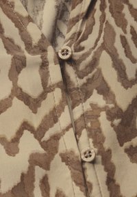 Camicia button-up marrone e beige con un motivo astratto, tessuto liscio e un dettaglio con un singolo bottone al colletto.