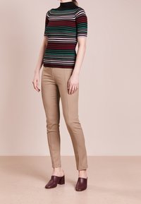 Geribbelde top met korte mouwen in rood, groen en zwarte strepen; beige slim-fit broek; donkerbruine gesloten instappers met een chunky hak.