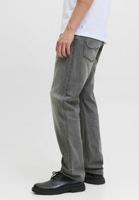 Jeans grii cu croială dreaptă, cu o texture uzată, design cu cinci buzunare și cusături contrastante, asortați cu pantofi negri cu șireturi.