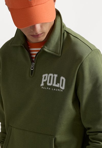 Olívazöld, cipzáras kapucnis pulóver magas gallérral, amelyen a mellkasán fehér "POLO RALPH LAUREN" logó található, valamint elöl egy kenguruzseb.