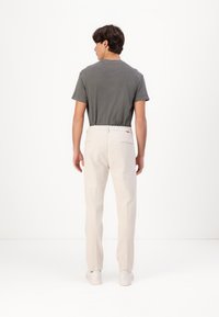 Grijze t-shirt met korte mouwen gecombineerd met lichtbeige broek. De broek heeft achterzakken en een lichte rekband. Witte sneakers.