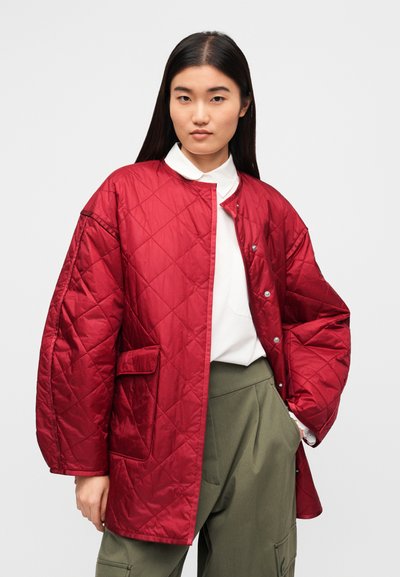 Κόκκινο μπουφάν με καπιτονέ σχέδιο, ψηλό γιακά και κουμπιά πατιλέτας. Διαθέτει μπροστινή τσέπη και φαρδιά μανίκια. Φοριέται πάνω από λευκό πουκάμισο και πράσινο παντελόνι.