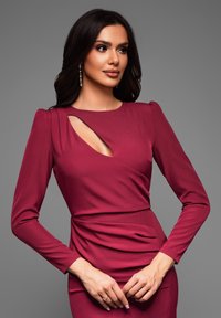 Robe longue bordeaux à manches longues avec un détail découpé à l'avant, présentant une silhouette ajustée et un tissu froncé à la taille. Texture lisse.