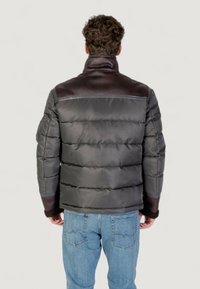Uomo che indossa un giubbotto imbottito grigio scuro con dettagli in pelle e jeans blu, visto da dietro su uno sfondo neutro.