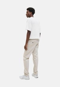 Weißes kurzärmliges T-Shirt, beiger Stoffhose und helle Sneakers. Lässige Passform mit sichtbaren Nähdetails und Taschen in der Hose.