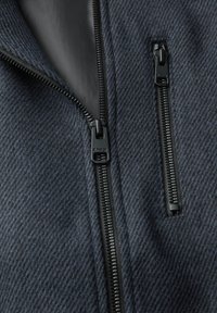 Close-up of dark gray textured fabric with two black zipper tracks, one partially open showing smooth inner lining.
