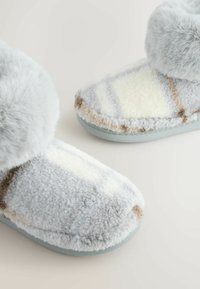 Graue Hausschuhe mit flauschigem Obermaterial, das cremefarbene und beige geometrische Muster aufweist. Weicher Stoff und gepolsterte Fütterung für Komfort. Gummisohle.