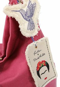 Borsa di tessuto rossa con etichette decorative: una con un colibrì blu su tessuto crema e l'altra con un'illustrazione del volto di Frida Kahlo.