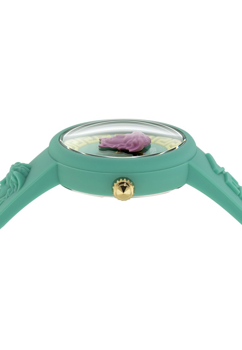 Montre en silicone turquoise avec un cadran rond, couronne en or et détail texturé violet sous le verre. Comprend un cadran à motif et un bracelet de forme.