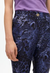 Pantaloni in stampa leopardata nelle tonalità di blu e nero, caratterizzati da una texture liscia, vita alta con un bottone dorato e dettagli con motivi animali.