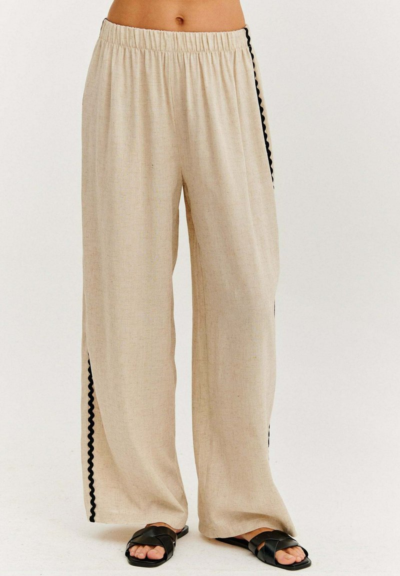 Béžové široké kalhoty z texturované tkaniny, s černým vykrojeným lemem podél bočních švů a elastickým pasem.