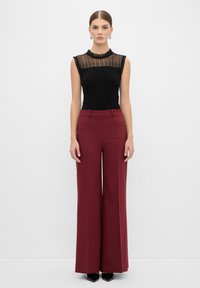 Zwarte geribbelde top met doorschijnende, gerimpelde halslijn; gecombineerd met brede bordeauxrode broek met twee achterzakken en verticale naden aan de voorkant.