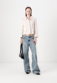 Svetlo roza skrajšana jakna z velikimi gumbi in dvema sprednjima žepoma, kombinirana s širokimi modrimi denim hlačami in majhno črno torbico.