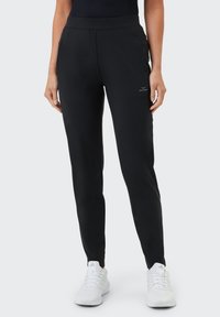 Schwarze Sporthose mit schlankem Schnitt, elastischem Bund, seitlichen Taschen und einem dezenten Logo auf der Vorderseite. Das Material wirkt glatt und leicht.