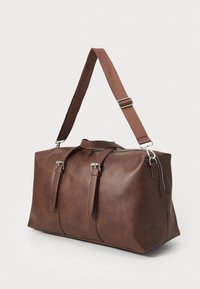 Bolso de viaje de cuero marrón con dos correas frontales, una correa para el hombro y un bolsillo lateral con cremallera. Textura suave con un diseño minimalista.