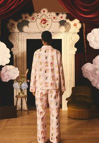 Růžový pyžamový set s hravým vzorem ilustrací inspirovaných cirkusem. Měkká tkanina s košilí na knoflíky a dlouhými kalhotami.