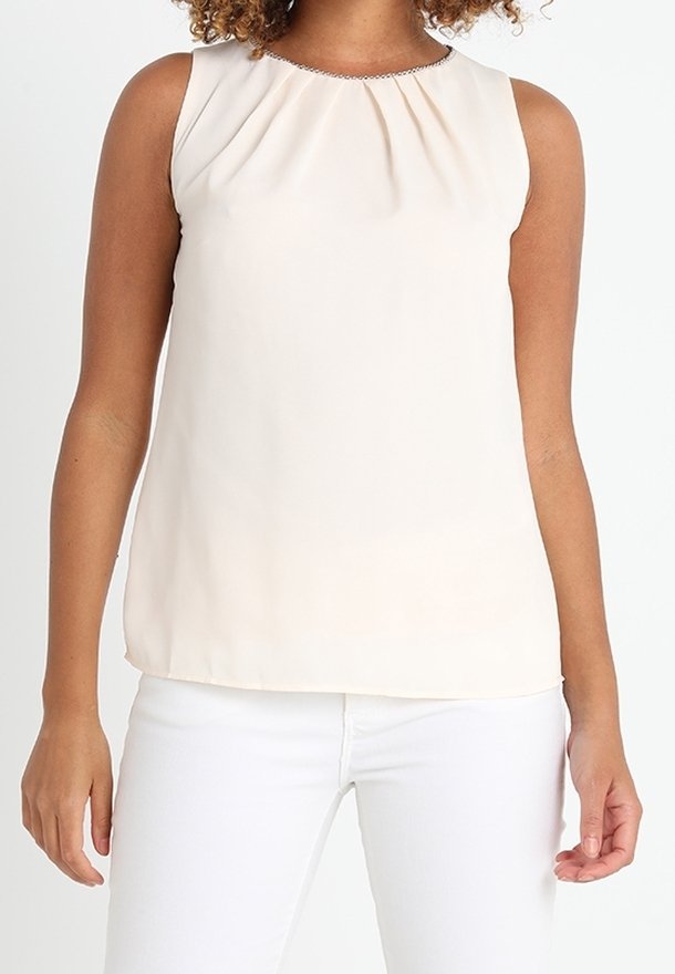Ærmeløs beige bluse med en samlet halsudskæring, glat tekstur og lige snit. Kombineret med hvide bukser, hvilket giver et afslappet look.