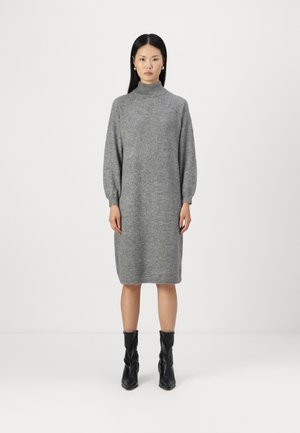 Robe en tricot gris avec un col haut, de longues manches bouffantes et une silhouette décontractée, associée à des bottines noires.