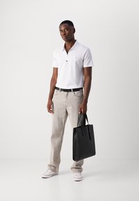 Hvid polo-shirt med lynlås krave, lysegrå jeans, sort bælte og en sort læder tote bag. Casual sneakers fuldender looket.