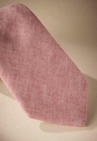 Cravate rose texturée avec un motif subtil, présentant une extrémité effilée et une surface en tissu lisse.