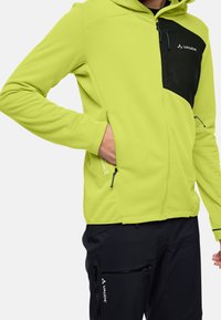 Giacca in pile verde con pannello anteriore nero, dotata di tasche con zip, cappuccio regolabile e polsini elastici. Logo visibile sul petto.