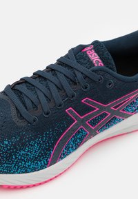 Baskets sportives avec une tige en mesh bleu foncé agrémentée de accents turquoise et rose, un design texturé, et une semelle blanche avec des détails roses.