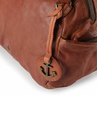 Bolso de mano de cuero marrón con un charm de ancla de bronce, bolsillo con cremallera, textura suave y forma redondeada.