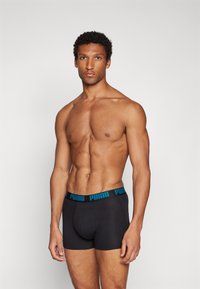 Black boxer briefs with a blue Puma logo waistband, made from soft, stretchy fabric. The style is fitted with a mid-rise cut.