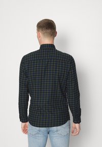 Rutigt button-up skjorta i marinblått och grönt med långa ärmar, krage och rundad fåll. Har kontrasterande sömmar och manschettknappar.